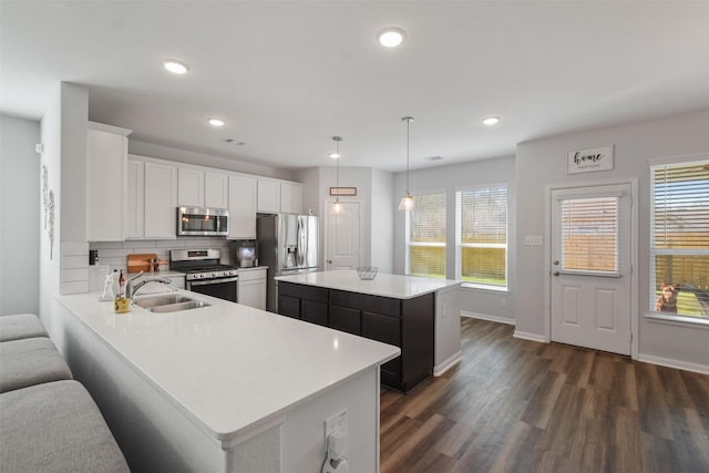 kitchen featuring a kitchen island, a sink, stainless steel appliances, dark wood-type flooring, and light countertops