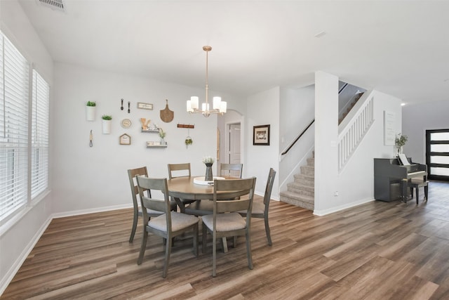 dining space featuring visible vents, baseboards, a chandelier, stairway, and wood finished floors