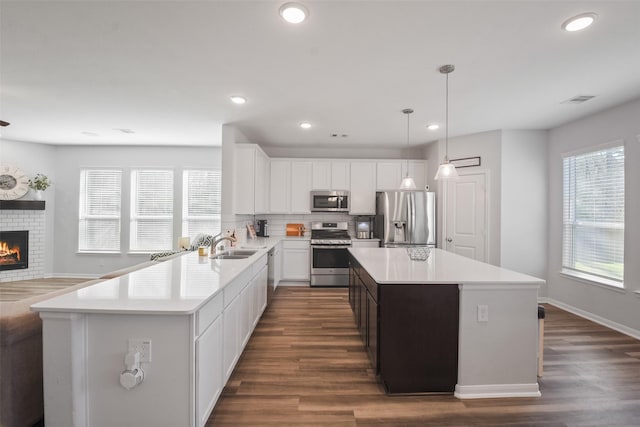 kitchen featuring visible vents, a sink, stainless steel appliances, light countertops, and a brick fireplace