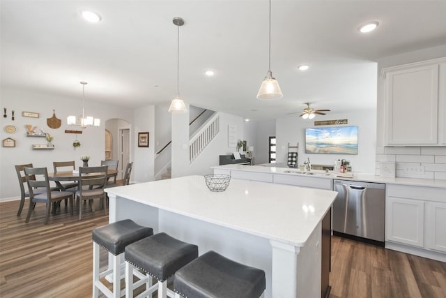 kitchen featuring stainless steel dishwasher, light countertops, arched walkways, and dark wood-type flooring