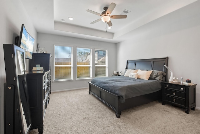 bedroom with visible vents, light colored carpet, a raised ceiling, and baseboards