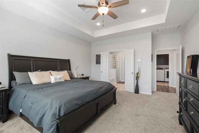 bedroom with visible vents, washer and dryer, light colored carpet, and a tray ceiling