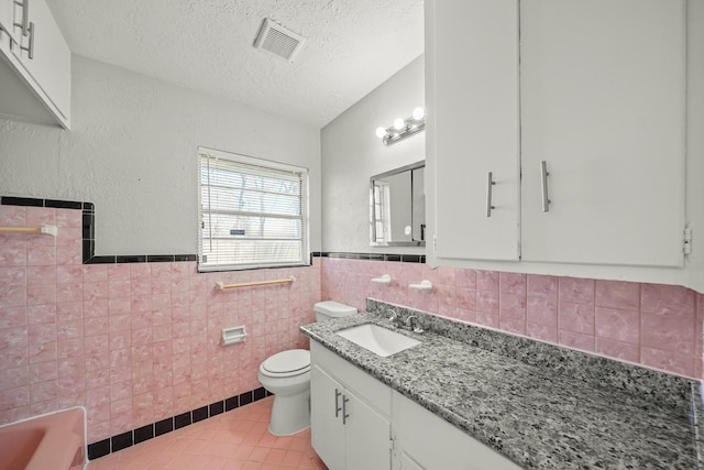 bathroom featuring visible vents, toilet, a textured ceiling, tile walls, and tile patterned flooring