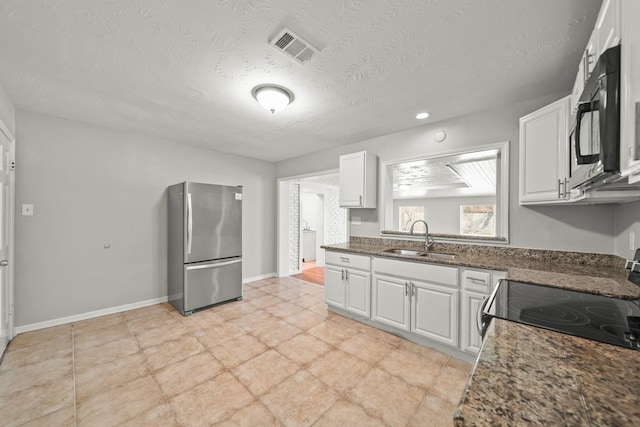 kitchen featuring visible vents, freestanding refrigerator, a sink, black microwave, and range with electric stovetop