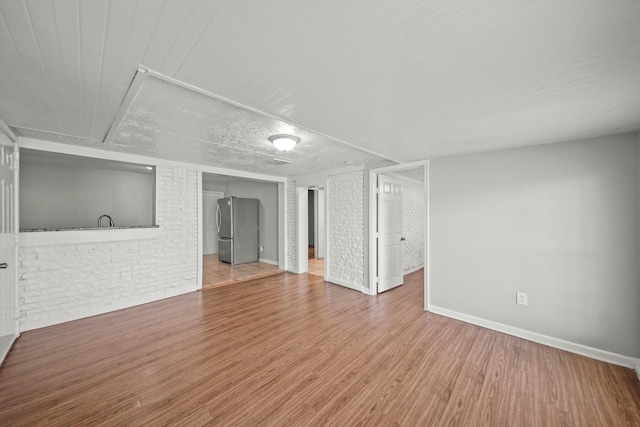 unfurnished living room featuring brick wall, baseboards, and wood finished floors