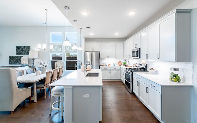 kitchen with dark wood-style floors, a sink, appliances with stainless steel finishes, a kitchen breakfast bar, and backsplash