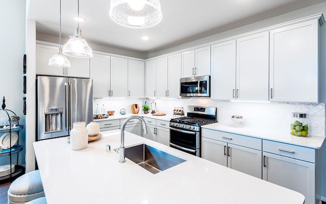 kitchen with a sink, appliances with stainless steel finishes, a breakfast bar area, light countertops, and hanging light fixtures