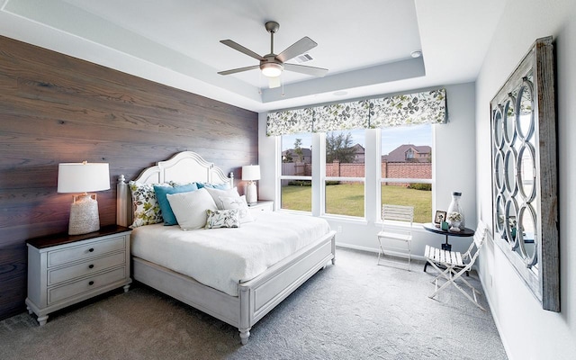 bedroom with wooden walls, a ceiling fan, baseboards, a tray ceiling, and carpet flooring