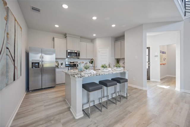 kitchen featuring visible vents, a breakfast bar, appliances with stainless steel finishes, light wood finished floors, and decorative backsplash