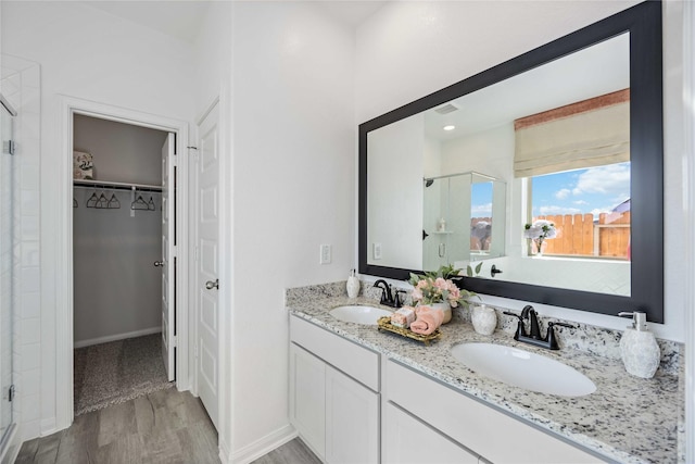 full bath with a sink, wood finished floors, a stall shower, and a spacious closet