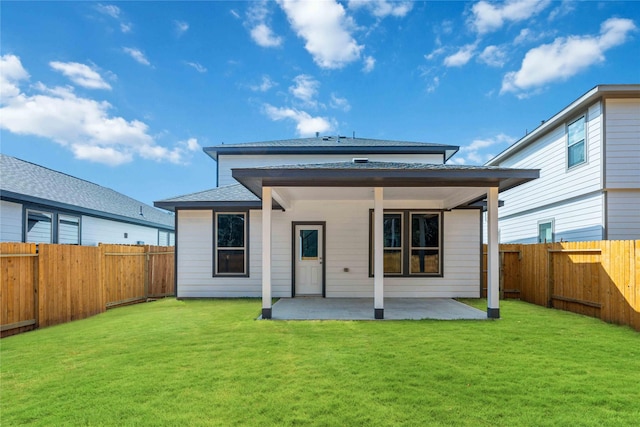 back of house featuring a yard, a patio, a fenced backyard, and a shingled roof