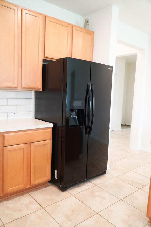 kitchen with backsplash, light brown cabinets, light countertops, light tile patterned floors, and black fridge with ice dispenser