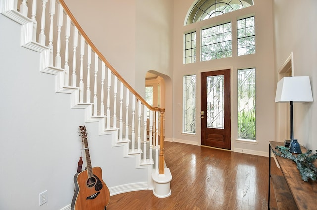 foyer entrance featuring arched walkways, baseboards, a towering ceiling, and wood finished floors