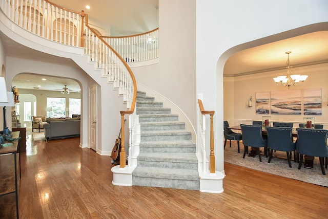 stairs featuring wood finished floors, baseboards, arched walkways, ornamental molding, and a towering ceiling