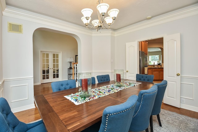 dining space with wood finished floors, visible vents, arched walkways, french doors, and a chandelier