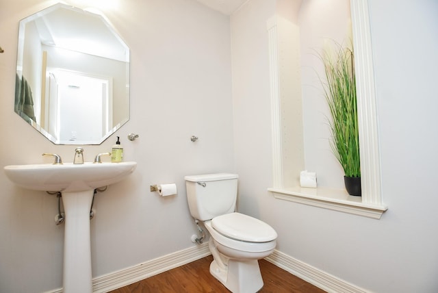 half bathroom with baseboards, toilet, and wood finished floors