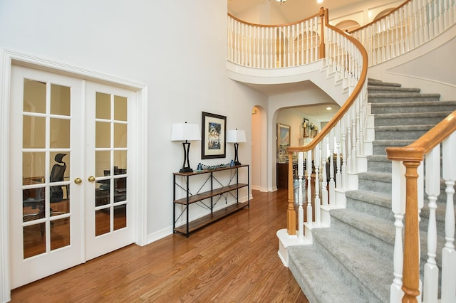 foyer featuring wood finished floors, french doors, arched walkways, baseboards, and a towering ceiling