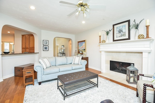 living room with a tiled fireplace, wood finished floors, arched walkways, and baseboards