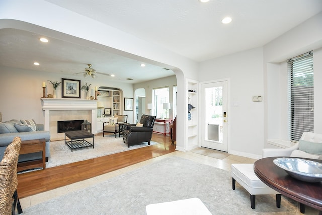 living area with recessed lighting, arched walkways, ceiling fan, a tiled fireplace, and tile patterned floors