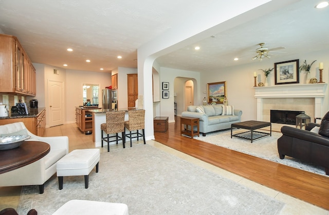 living area with light wood-type flooring, a ceiling fan, recessed lighting, arched walkways, and a fireplace