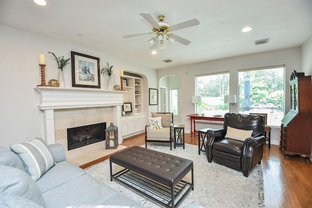 living room with built in features, wood finished floors, visible vents, a fireplace, and arched walkways