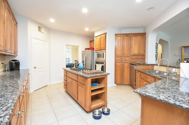 kitchen featuring visible vents, a kitchen island, appliances with stainless steel finishes, arched walkways, and a sink