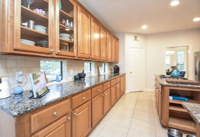 kitchen featuring glass insert cabinets, dark stone counters, light tile patterned floors, decorative backsplash, and recessed lighting