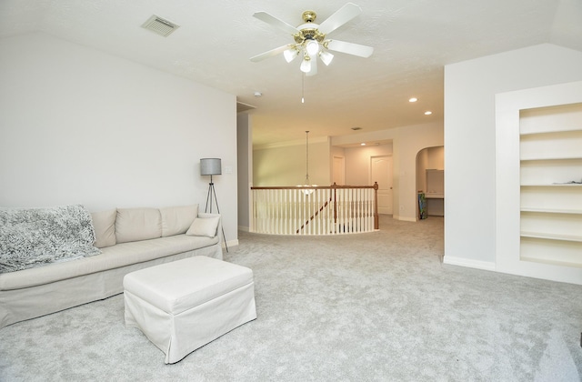 living room featuring built in shelves, carpet, visible vents, baseboards, and arched walkways