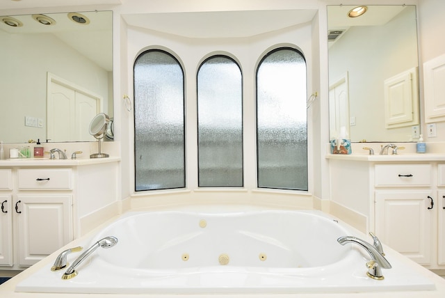 full bath with visible vents, a jetted tub, and two vanities