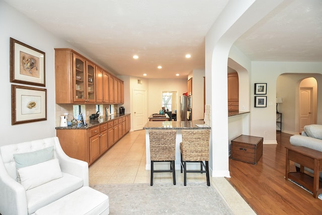 kitchen with glass insert cabinets, arched walkways, a kitchen breakfast bar, light tile patterned flooring, and brown cabinetry