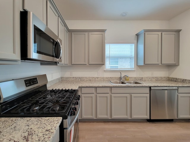 kitchen with light wood-style flooring, gray cabinetry, stainless steel appliances, and a sink