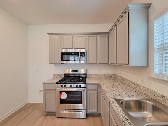 kitchen with baseboards, light wood finished floors, gray cabinets, a sink, and stainless steel appliances