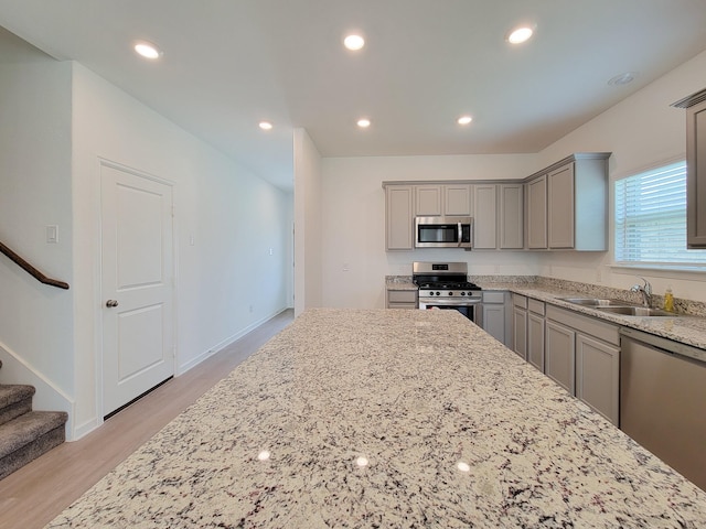 kitchen with gray cabinets, a sink, recessed lighting, appliances with stainless steel finishes, and light stone countertops