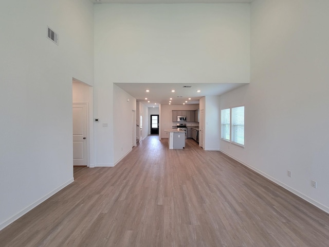 unfurnished living room with visible vents, a high ceiling, light wood-type flooring, and baseboards