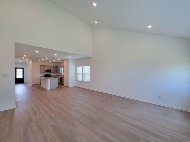 unfurnished living room with recessed lighting, baseboards, a high ceiling, and light wood-style flooring