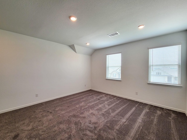 spare room featuring dark colored carpet, visible vents, baseboards, and a textured ceiling