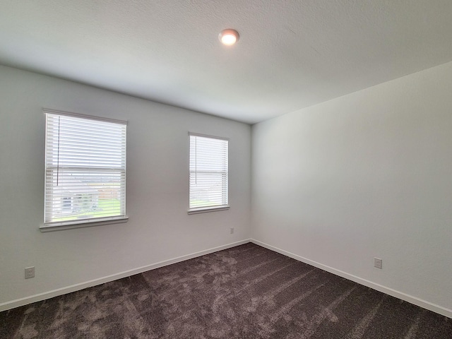 spare room featuring baseboards and dark carpet