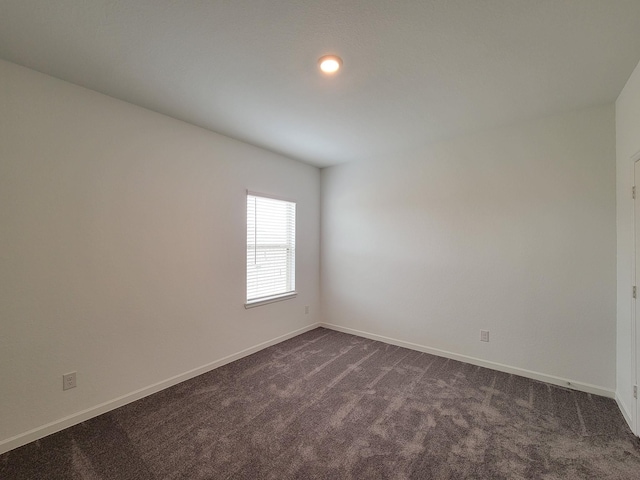 unfurnished room featuring dark colored carpet and baseboards