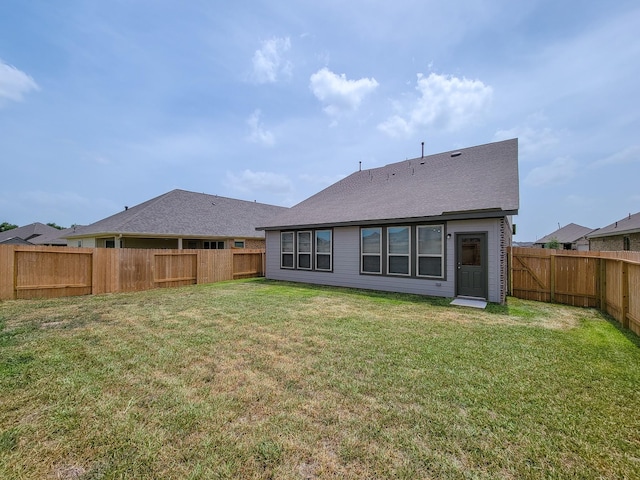 rear view of property featuring a lawn and a fenced backyard