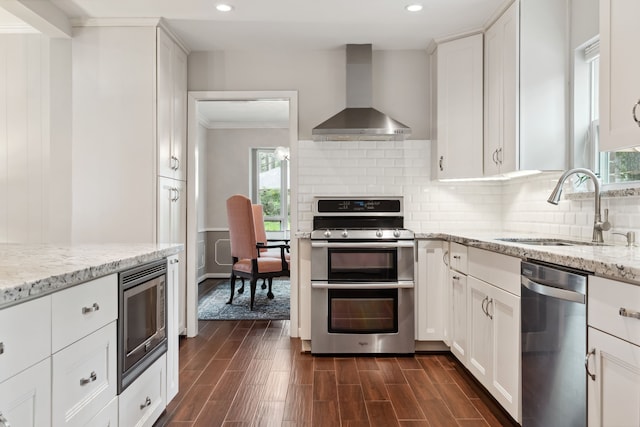 kitchen with a sink, backsplash, appliances with stainless steel finishes, wall chimney exhaust hood, and dark wood-style flooring