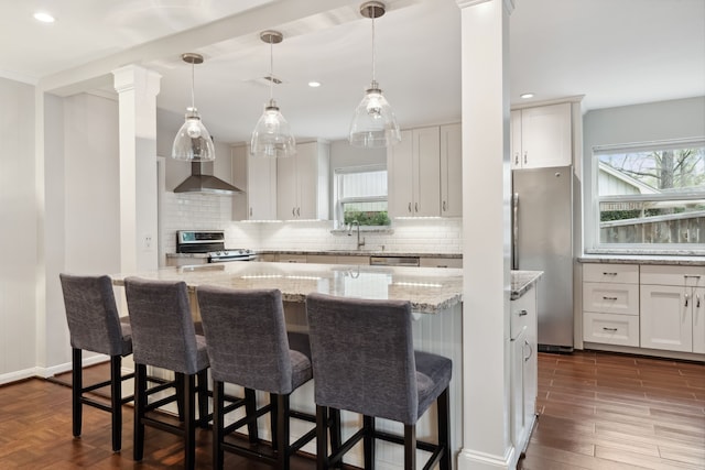 kitchen featuring visible vents, a kitchen island, appliances with stainless steel finishes, white cabinets, and wall chimney exhaust hood