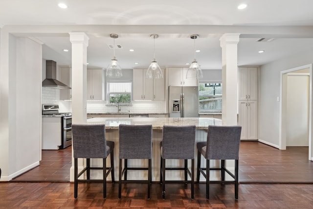 kitchen featuring stainless steel appliances, wall chimney exhaust hood, ornate columns, and a sink