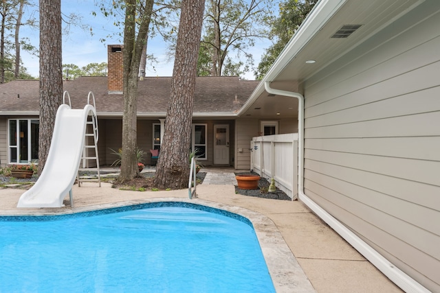 outdoor pool with a patio area, fence, and a water slide