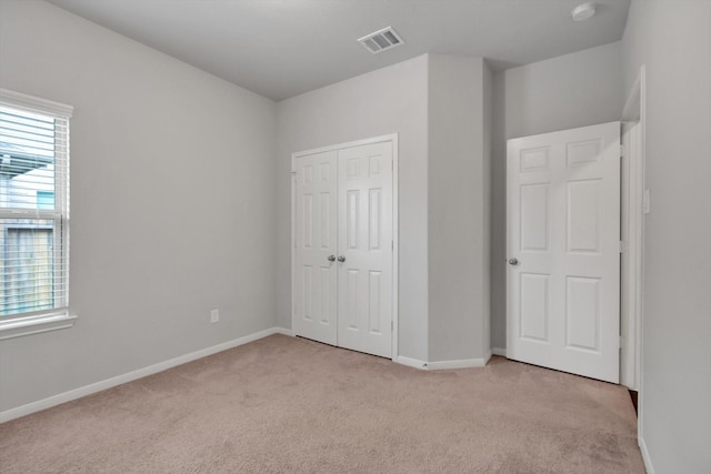 unfurnished bedroom featuring visible vents, baseboards, light colored carpet, and a closet