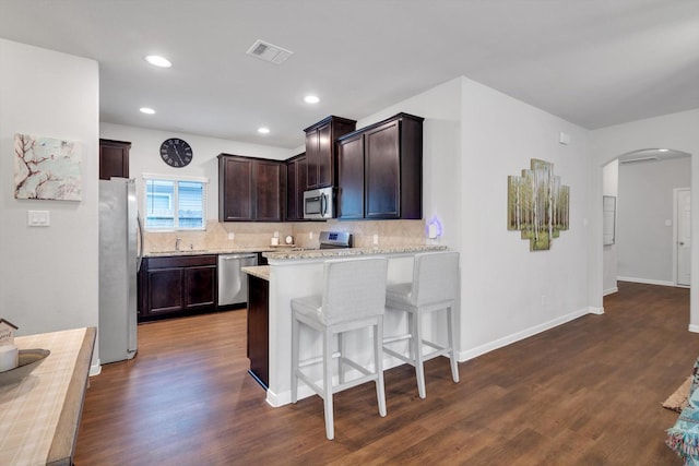 kitchen with visible vents, arched walkways, appliances with stainless steel finishes, dark brown cabinets, and dark wood-style flooring