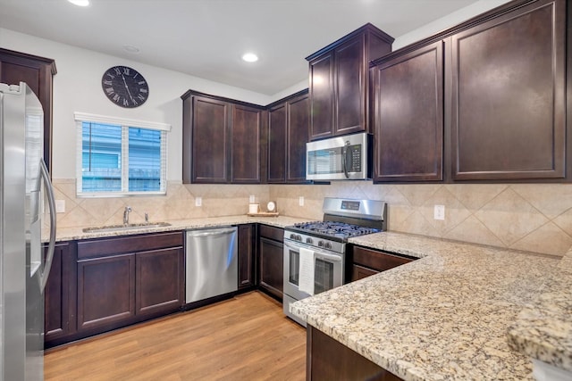 kitchen featuring light stone countertops, decorative backsplash, light wood-style flooring, stainless steel appliances, and a sink