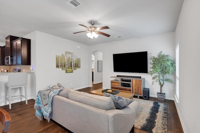 living room with visible vents, arched walkways, dark wood-style flooring, and a ceiling fan