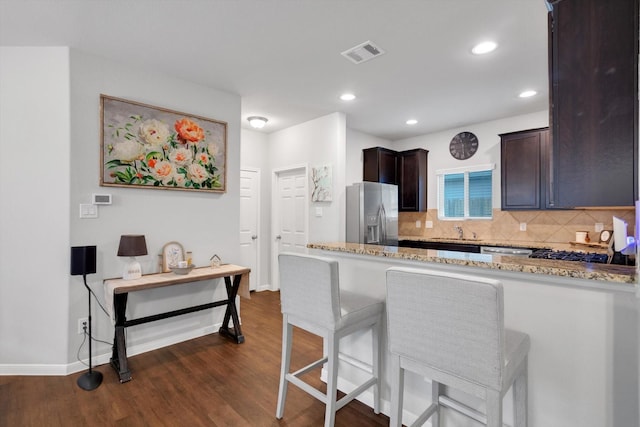 kitchen with dark wood-style floors, light stone counters, stainless steel fridge with ice dispenser, and visible vents