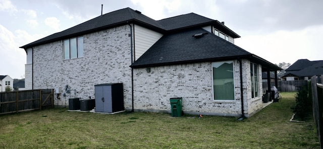 rear view of house with cooling unit, a lawn, brick siding, and fence