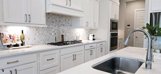 kitchen with premium range hood, decorative backsplash, stainless steel appliances, white cabinetry, and a sink